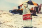 An empty coca cola logo half-buried in sand